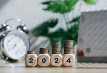 Budget 2024 with blurred office background. Wooden cubes with 2024 and goal icon on coins stack....