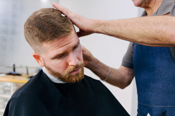 Fototapeta premium Young redhead man shaving his beard in the barbershop