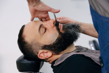 Fototapeta premium Man shaving his beard with razor in the barbershop