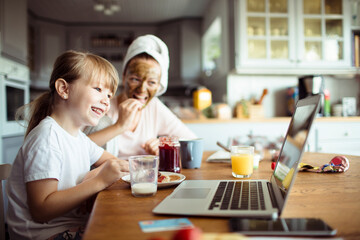 Daughter having breakfast with mother and using laptop