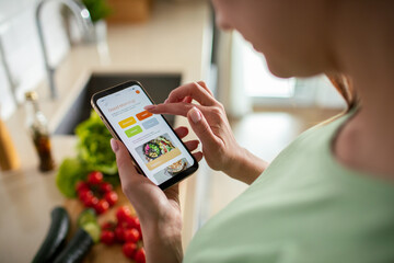 Young woman using recipe app on smartphone for preparing meal at home