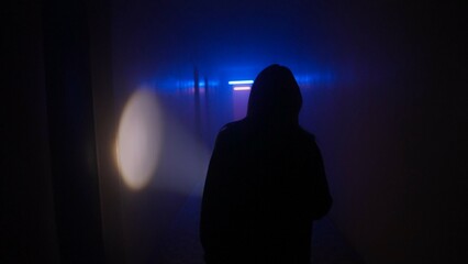 Portrait of female in the dark hallway with neon light. Woman with flashlight facing the camera walking down alone in the corridor.