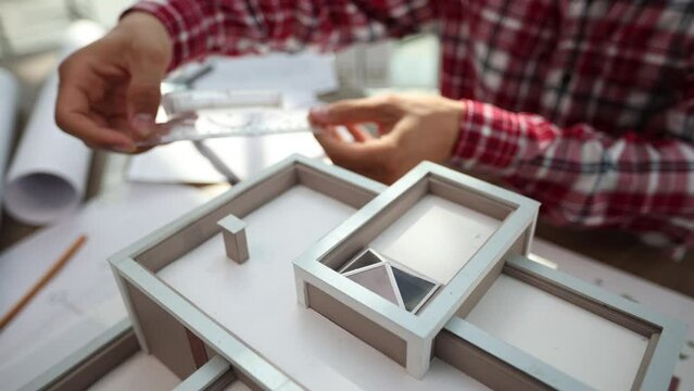 young male designer assembling wooden pieces into a house model
