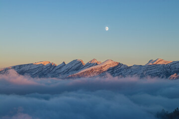 sunset in mountains with see of clouds and moon