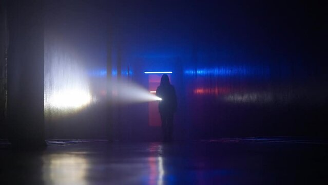 Portrait of female in the dark hallway with neon light. Shot from the ground girl with flashlight walking to the camera facing it.