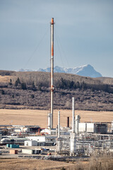 Rural Alberta gas plant with flare stack and industrial equipment portrait view overlooking hillside and mountain near Cochrane Alberta Canada..