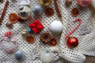 Various colorful Christmas ornaments, small presents and seasonal spices on white knitted blanket. Top view.
