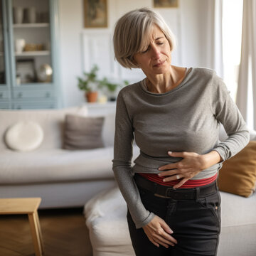 Femme qui a des douleurs au ventre et je tiens les mains sur l'estomac le visage crisp&eacute;, elle est debout dans son appartement