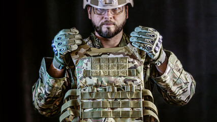 soldier in camouflaged uniform and tactical gloves holding military armored vest