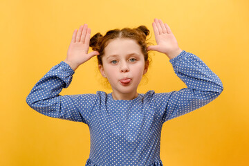 Portrait of funny preteen girl child sticking out tongue and grimacing looking at camera, holding...