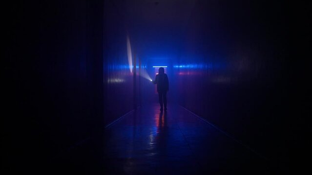 Portrait of female in the dark hallway with neon light. Low ground shot woman with flashlight walking down the basement tunnel.