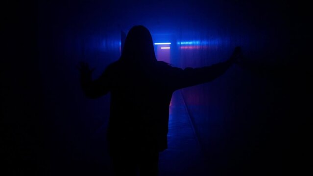 Portrait of female in hallway blue neon light. Close back shot woman walking cautiously in the dark corridor, holding up to wall.