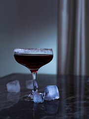 A martini glass with a sugar edge and ice on a marble table against a background of a satin curtain