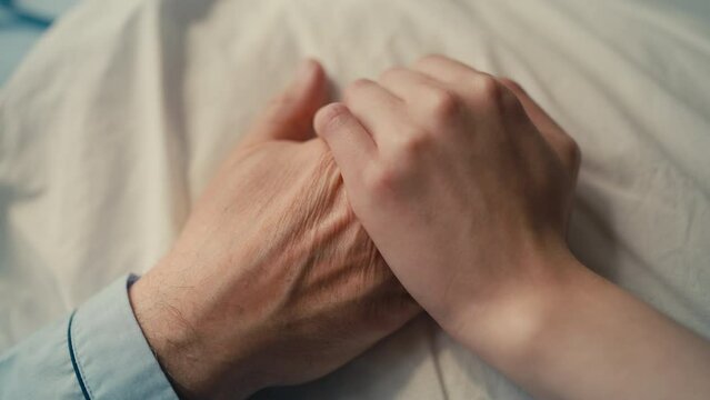 Daughter supporting terminally ill father lying in nursing home bed, family care