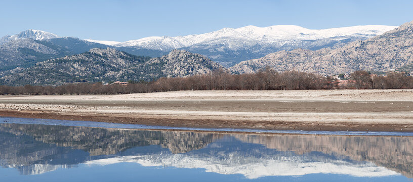 A panoramic view of a serene lake with snow-capped mountains in the background and a clear reflection in the water