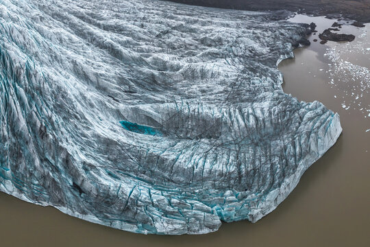 From above aerial shot showcasing a glacier coursing through Vatnajokull National Park in Iceland, surrounded by rugged terrain