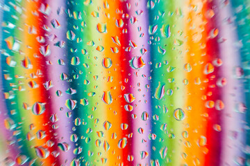 Water droplets on a glass surface with a blurred background showcasing a spectrum of colors in vertical lines