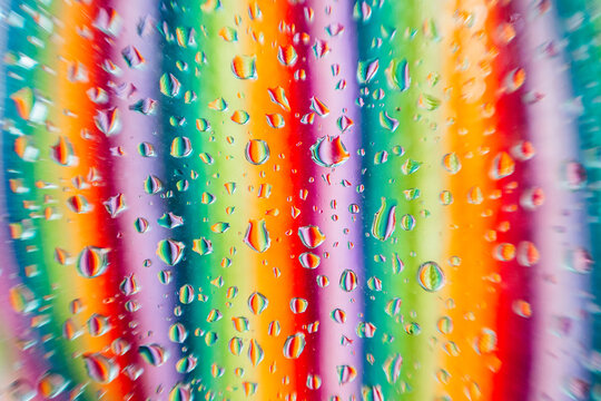 Water droplets on a glass surface with a blurred background showcasing a spectrum of colors in vertical lines
