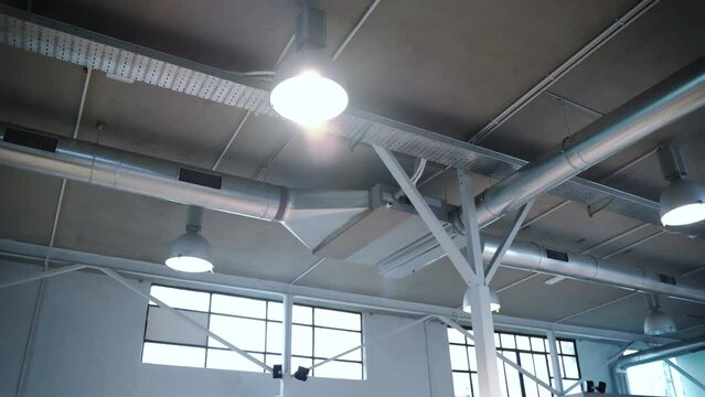 Bottom view of modern installed ventilation system in loft space with big windows and ceiling hanging lamps, metal pipes cooling space room, engineering project concept