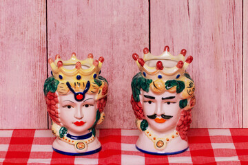 Souvenir from Sicily. Traditional sicilian ceramic pots or vases with heads of a couple of lovers of Moorish heads on red checked napkin of wooden wall.