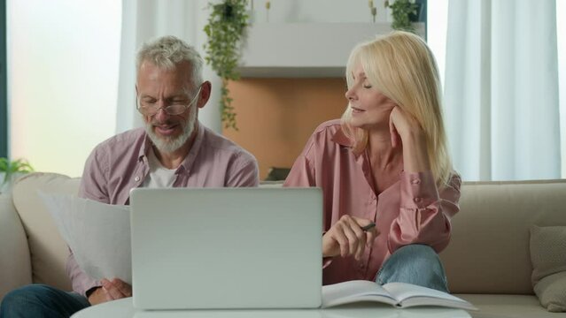 Satisfied family couple Caucasian man woman grandparents customers talking checking papers documents using laptop planning budget investment loan insurance payment at home paid debt successful deal
