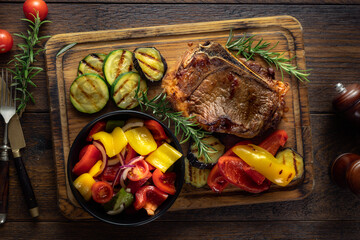 Juicy cooked grilled beef steak with vegetables on a wooden cutting board on a dark stone...