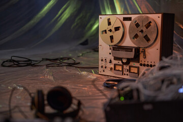 Part of studio interior in dim light with focus on vintage reel-to-reel magnetic tape recorder on floor covered with plastic