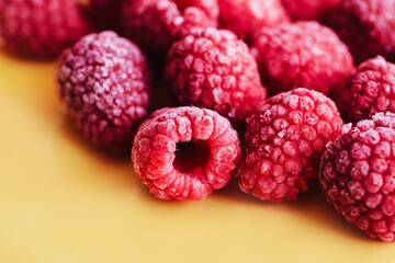 Frozen raspberries background. Closeup fruits on yellow. Vivid vibrant color fruit background. Group of berries.