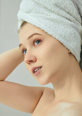 A lovely woman with freckles with her hair wrapped in a white towel enjoys cleanliness after a shower