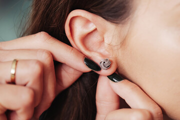 Silver earrings background. Closeup woman ear. Putting on earrings. Silver ball stud. Shiny...