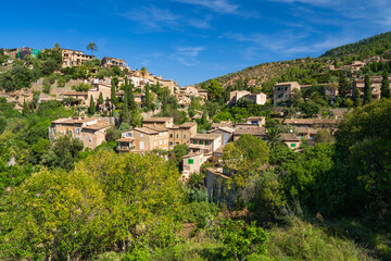 Fototapeta na wymiar Stunning cityscape of the small coastal village of Deia in Mallorca, Spain. Traditional houses terraced on hills surrounded by green trees. Tourist destinations in Spain. Balearic Islands.