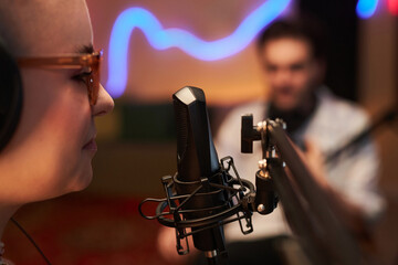 Close up shot with side view of young girl podcaster speaking into microphone in studio