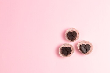 Three chocolate candy hearts in paper cups on a pink background