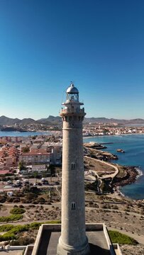 Vertical video of the Cabo de Palos lighthouse in Murcia, Spain. Costa Calida, mediterranean tourism. Beaches and coves on a sunny day.
