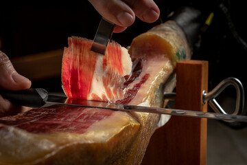 Close up of gourmet cutter slicing acorn fed iberian ham. Spanish delicatessen food.