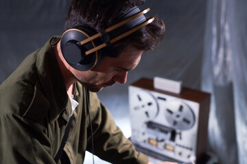 Medium close up shot of adult male sound producer in headphones looking down while making analog...
