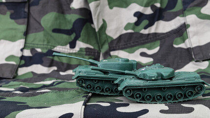 Plastic toy tank on the background of military camouflage. The concept of Russia's war against Ukraine.