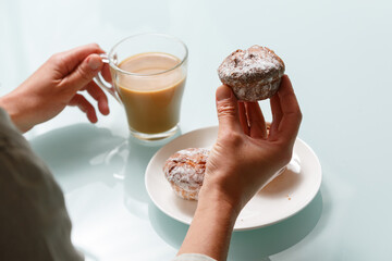 Close up of hands holding curd muffin and glass cup of coffee with milk.