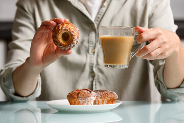 close up of hands  holding curd muffin and glass cup of coffee with milk over plate with another cakes