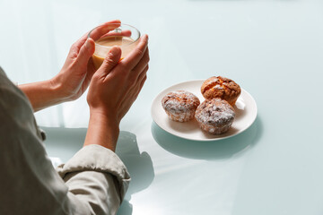 Close up of hands holding glass cup of coffee with milk and three curd muffins on plate