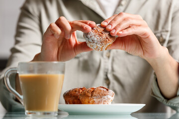 close up of hands  holding curd muffin over plate with two another cakes, and glass cup of coffee...