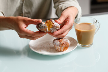 close up of hands breaking apart one of two curd muffins over plate, and glass cup of coffee with...