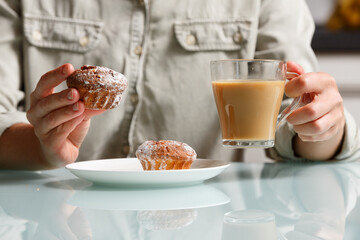close up of right hand taking one of two curd muffins from plate, and left hand holding glass cup...