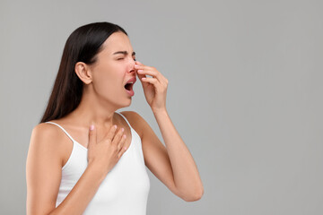 Suffering from allergy. Young woman sneezing on light grey background, space for text