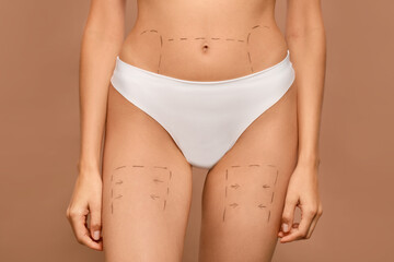 Fototapeta na wymiar Slim woman with markings on body before cosmetic surgery operation on light brown background, closeup
