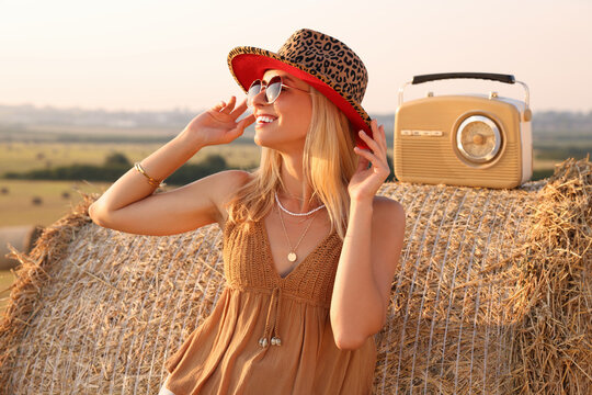 Happy hippie woman with receiver near hay bale in field