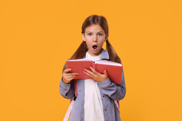 Emotional schoolgirl with open book on orange background