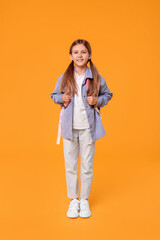 Happy schoolgirl with backpack on orange background