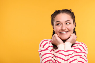 Smiling woman with braces on orange background. Space for text - obrazy, fototapety, plakaty