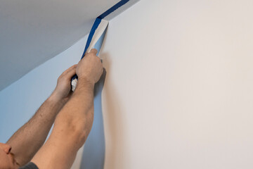 Precision Unveiled: Man's Hands Skillfully Remove Paint Tape, Revealing Pristine Room Corners.